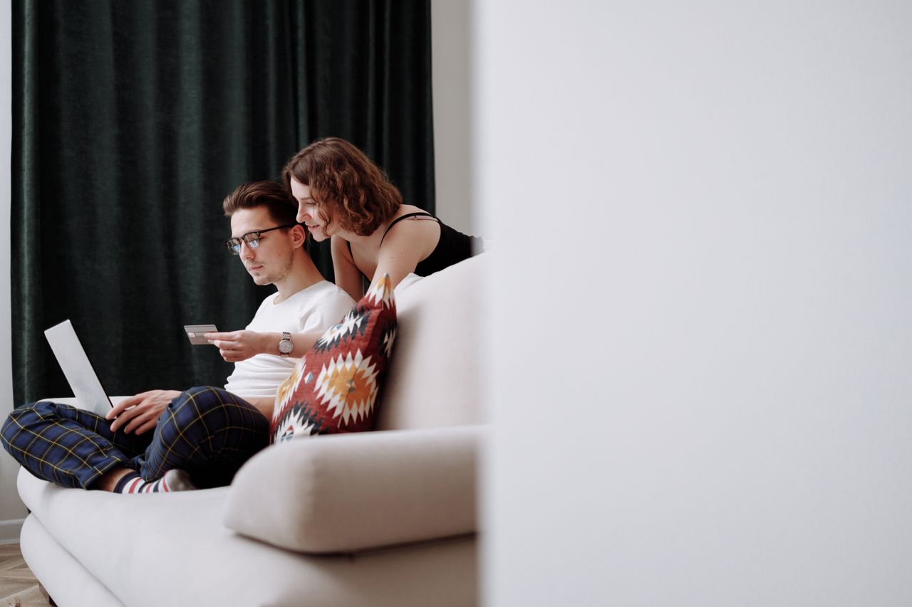 About A couple sits comfortably on the couch while shopping online together.